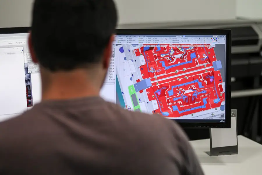 Projetista a trabalhar numa placa de molde em 3D, cavidades a vermelho e azul