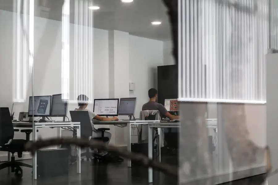 Equipa de projeto a trabalhar em CAD, vista através da parede de vidro do gabinete